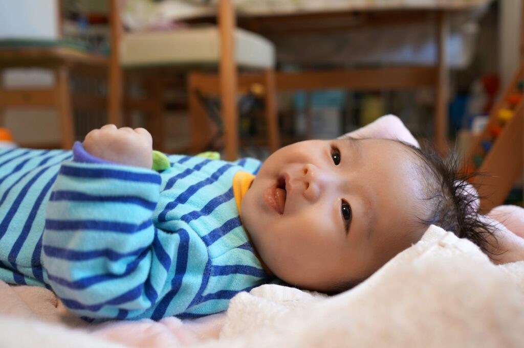 リビングで寝そべるロンパースを着た笑顔の赤ちゃん